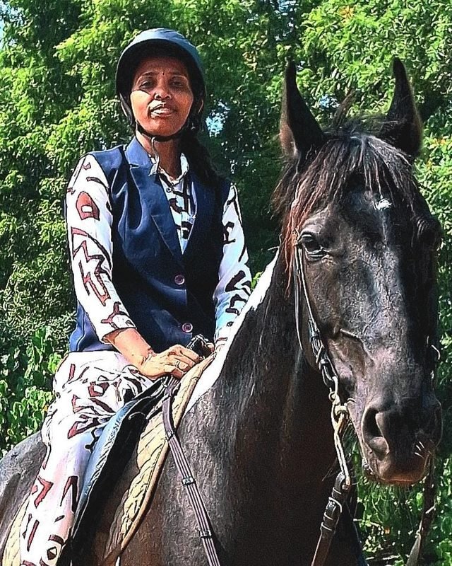 Mrs. Ezhilarasi Jayaraman in riding helmet and vest, mounted on a dark native horse at Shri Surya Horse Riding Training Centre
